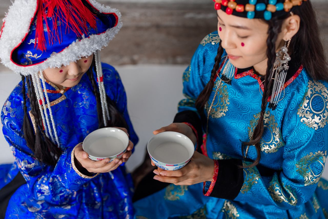 hero-img-01 Mother and daughter in Mongolian attire sharing a cultural drink ceremony.